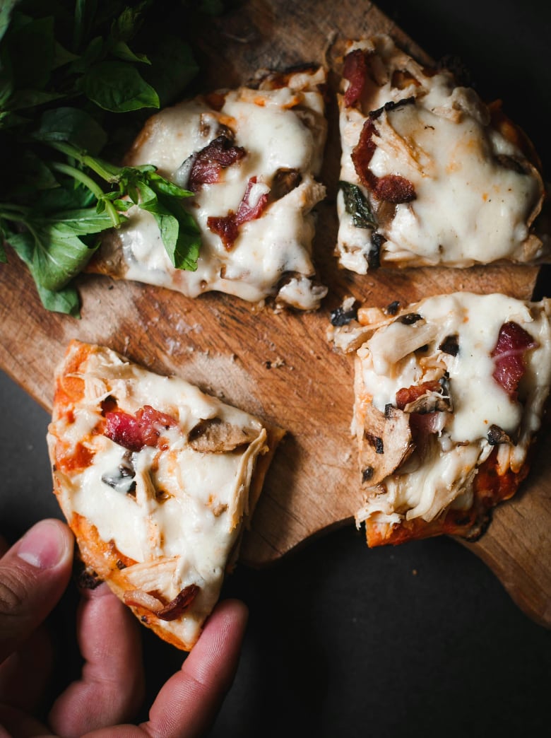 Hand holding a slice of wood-fired pizza topped with mushrooms, prosciutto and fresh basil