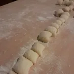 Fila di gnocchi di patate fatti a mano allineati su una tavola di legno infarinata