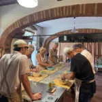 Partecipanti al corso di cucina che impastano pasta fresca insieme in una cucina di fattoria toscana
