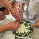 Mani che mescolano il ripieno di ricotta e spinaci per la pasta fresca durante un corso di cucina