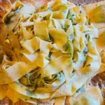Primo piano di tagliatelle fresche decorate con erbe pressate, spolverate di farina