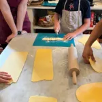 Bambino che taglia le tagliatelle fresche da un foglio di pasta durante un corso di cucina in famiglia nel Chianti